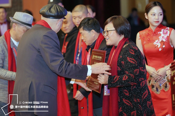 上海市家具研究所副所長許美琪（左一）為祥瑞坊紅木頒發“2019闊葉黃檀家具熱門品牌”獎牌，祥瑞坊紅木董事長賀瓊燕（右一）上臺領獎