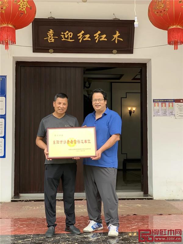 東陽市消費者協會秘書長韋響亮與喜迎紅紅木董事長陸飛躍（左一）合影留念